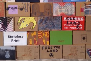 OUR LAND sign screenprinted on a cardboard box, displayed in The State of Print exhibition